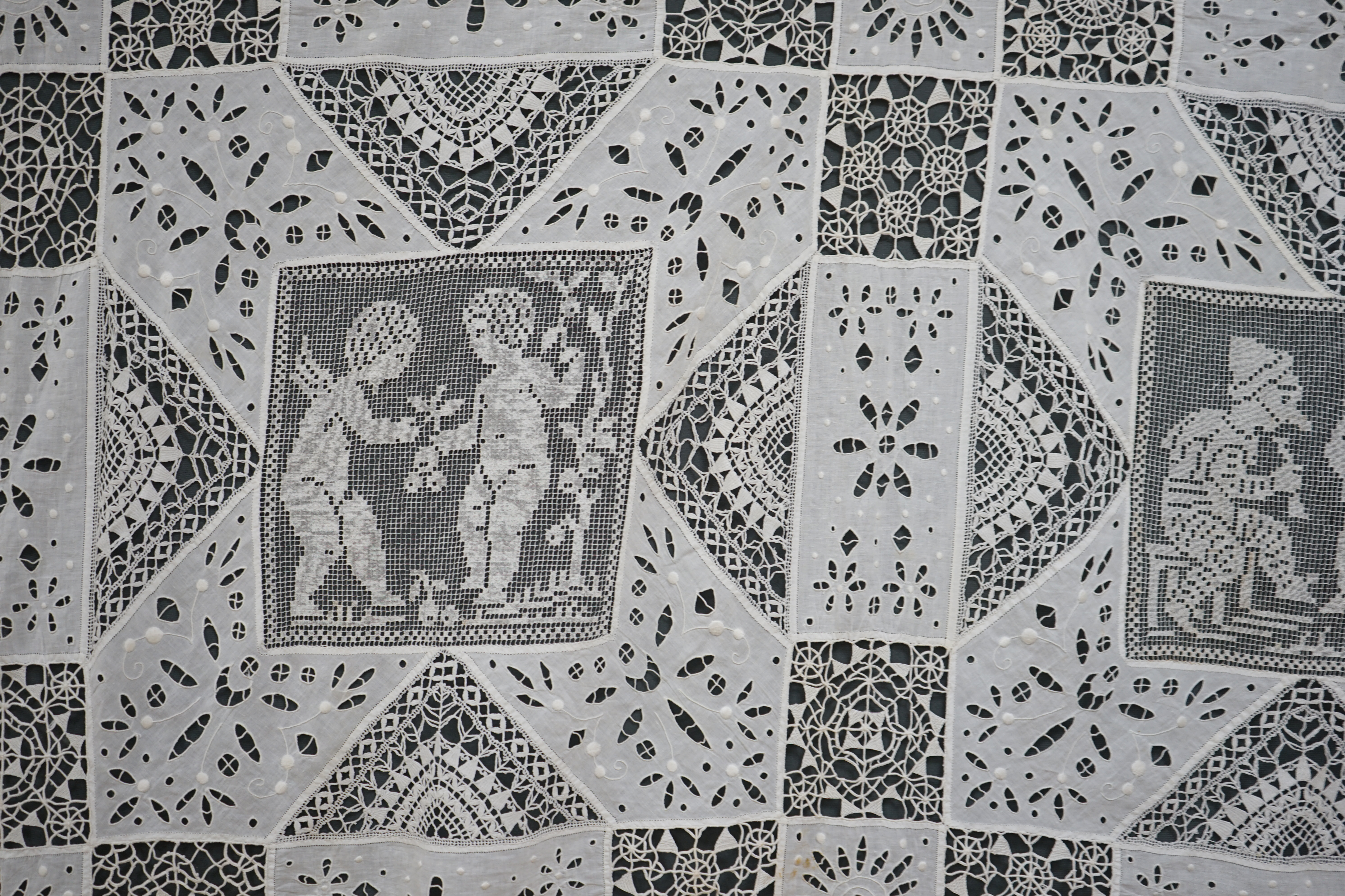 An early 20th century Italian ornate bedcover, worked with square fillet lace insertions of putti, white multi patterned cut work squares on fine linen and similar multi patterned needle lace squares, creating a unique b